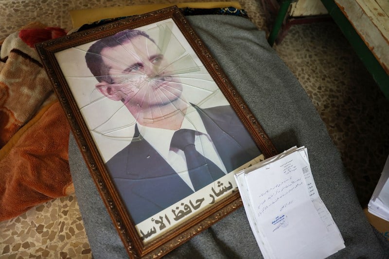 A framed picture of Bashar al-Assad is seen with its glass shattered on the ground.