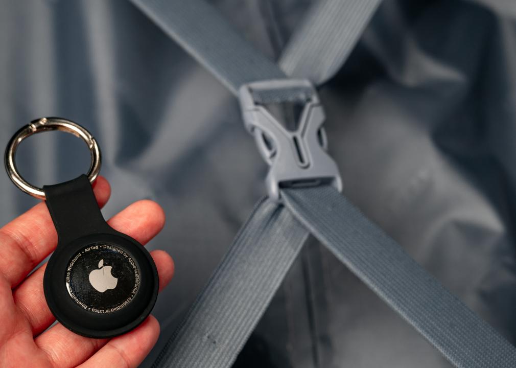 Apple AirTag held in someone's hand with their luggage in the background.