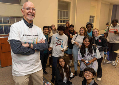 Professor stands with arm crossed in classroom alongside a group of students