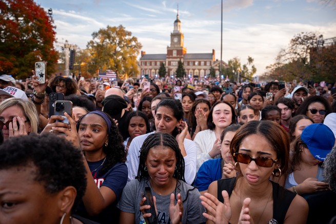 A crowd of people, facing the camera, are upset and crying at a Kamala Harris rally after she lost the 2024 presidential election.