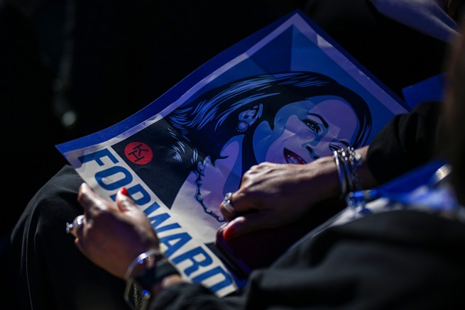 A person holds a Kamala Harris sign in their lap.