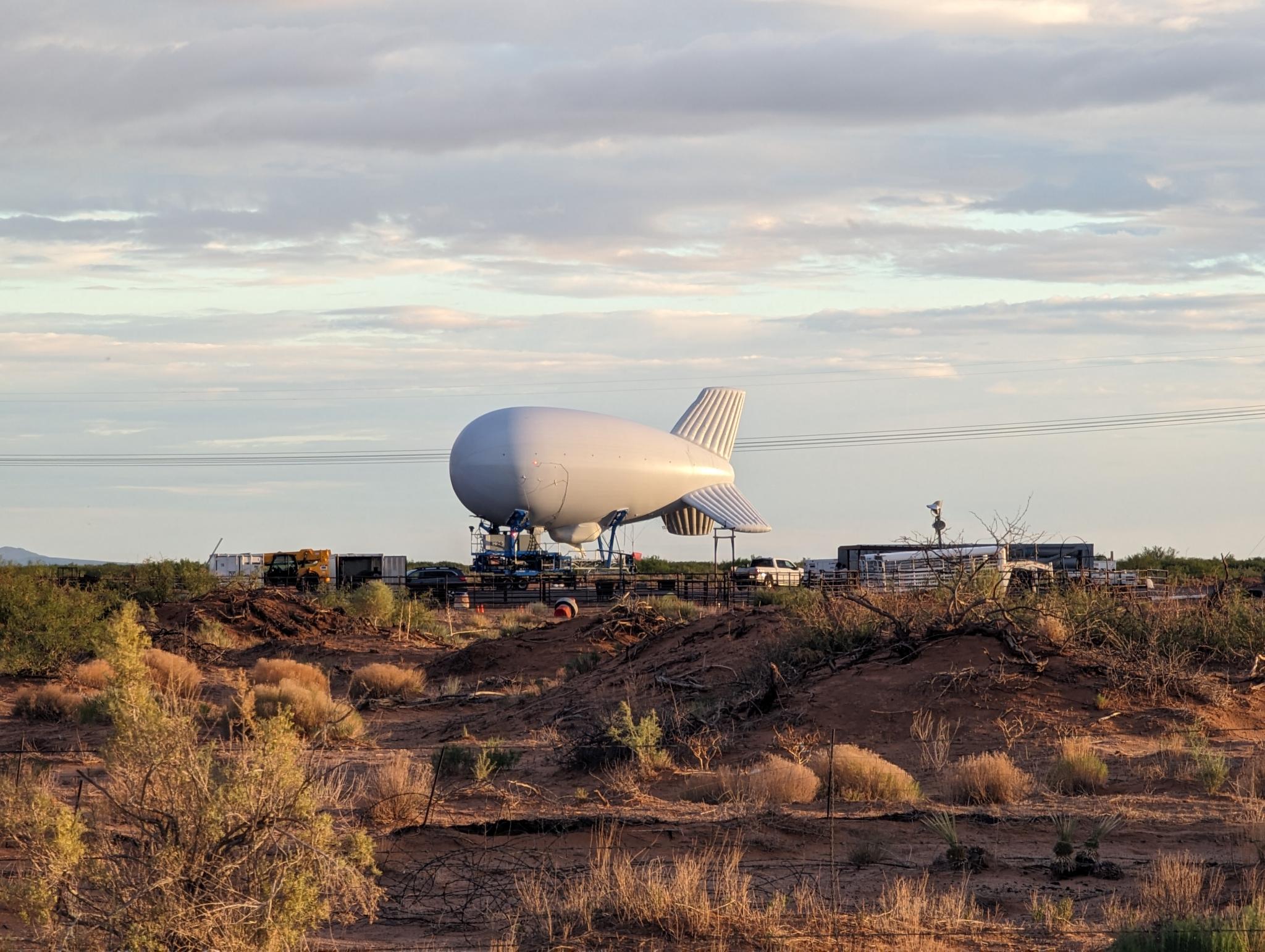 A white blimp on the ground in the middle of the desert. 