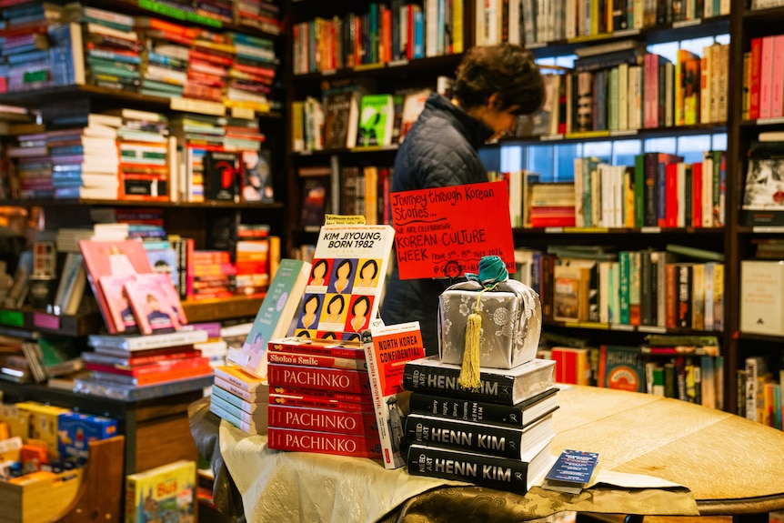 A stack of Korean books on a table with a person browsing in the background among out-of-focus books.