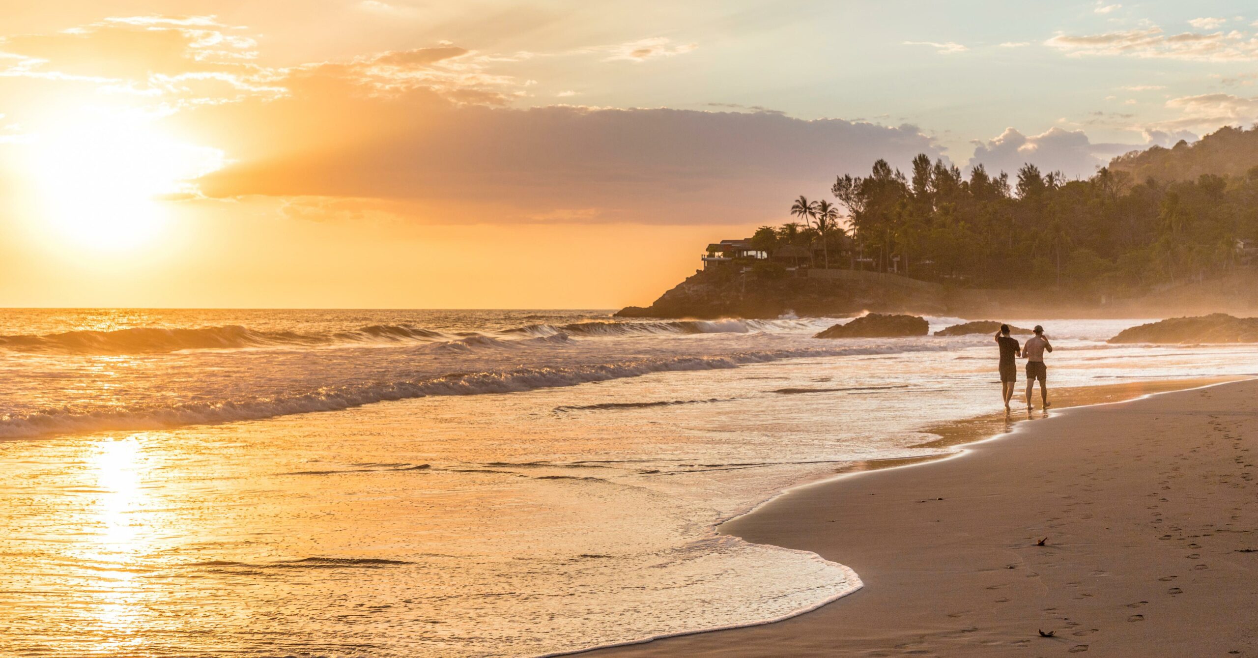 Sunset over El Zonte beach in El Salvador, with two people walking along the shore.