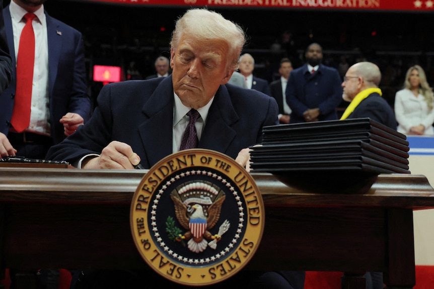 Donald Trump sits at a desk and signs an executive order during his inauguration.