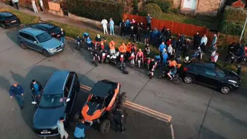 Westroyd Movement Aerial shot of young people gathered in a street with motorbikes and quad bikes