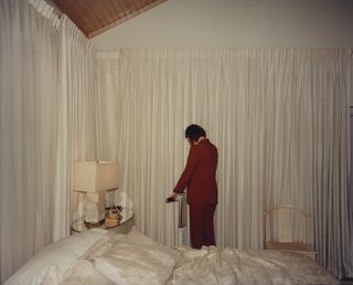 actress Emma Stone standing next to a bed in front of a white curtain