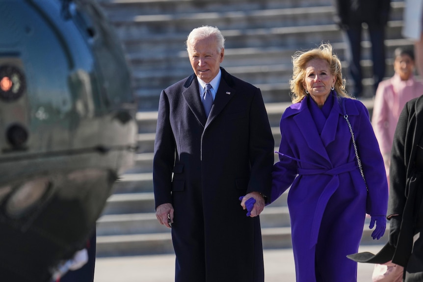 Joe Biden and Jill Biden, dressed in a purple coat, walk towards a waiting helicopter