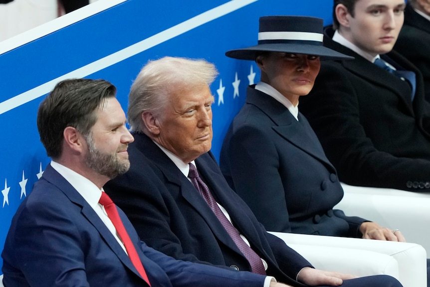 Donald Trump sits with JD Vance, left, and first lady Melania Trump, who wears a stylish blue hat low on her face.