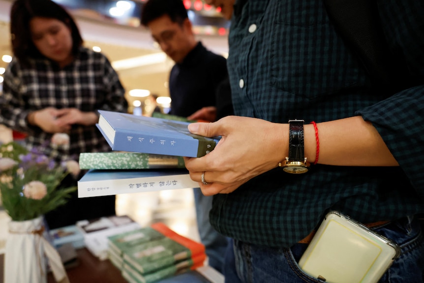 A close up of a person's hand holding three books with Korean text. The person wears wedding ring, watch and red cotton on wrist