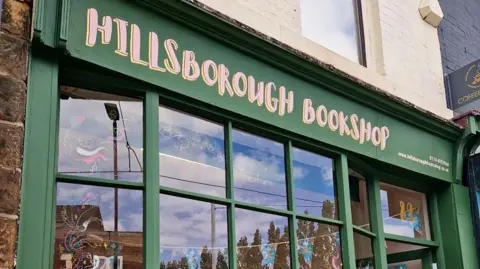 Sophie Rowe A green bookshop window at the front of the building with pink writing that reads: Hillsborough Books.