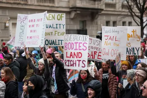 Getty Images Protesters hold signs. One reads 