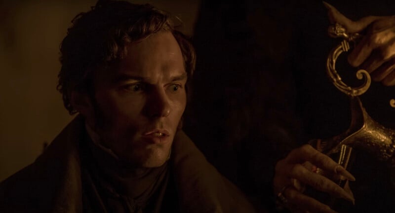 A dimly lit scene with a person gazing intently to the side, illuminated by a warm light. A hand holding an ornate, golden object with a dragon-shaped design is visible in the foreground. The atmosphere is tense and dramatic.