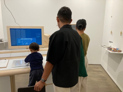 Two adults and a child in front of an interactive vintage computer console in a museum gallery