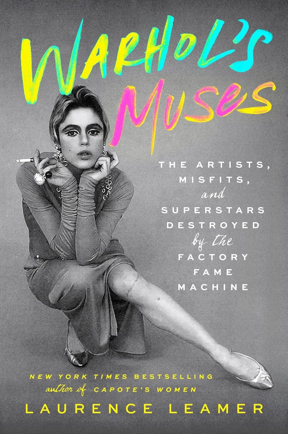 An image of the book cover for Warhol’s Muses by Laurence Leamer. The cover features a black-and-white photograph of Edie Sedgwick, one of Andy Warhol’s muses, sitting and smoking a cigarette, with neon-colored title text.