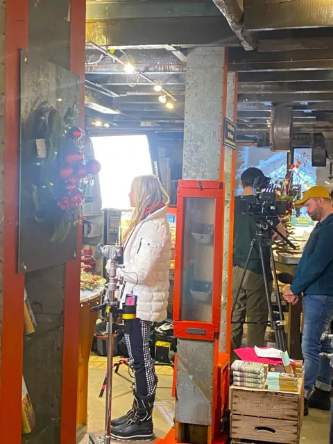 John Argo/The Watermill Actress Caprice stands on set during filming in the café while crew members set up cameras. 