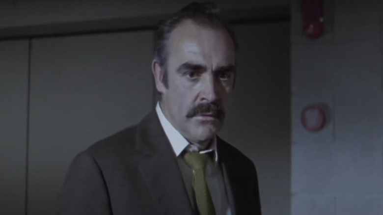 Sean Connery's Detective Sergeant Johnson looks worried as he stands against a grey background in The Offence