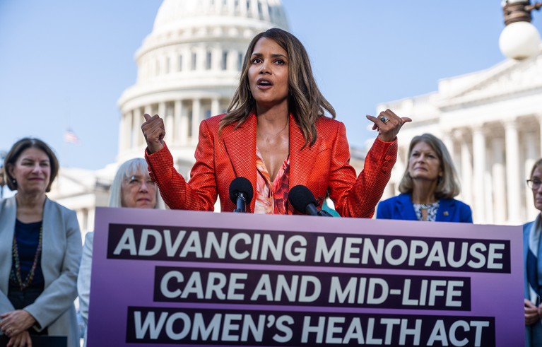 Halle Berry speaking from a podium with US Capitol and a few women in the background.