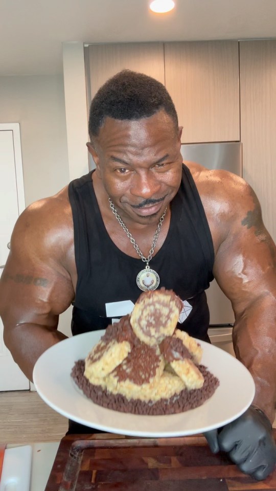 A muscular man in a black tank top presenting a plate of chocolate-covered treats.