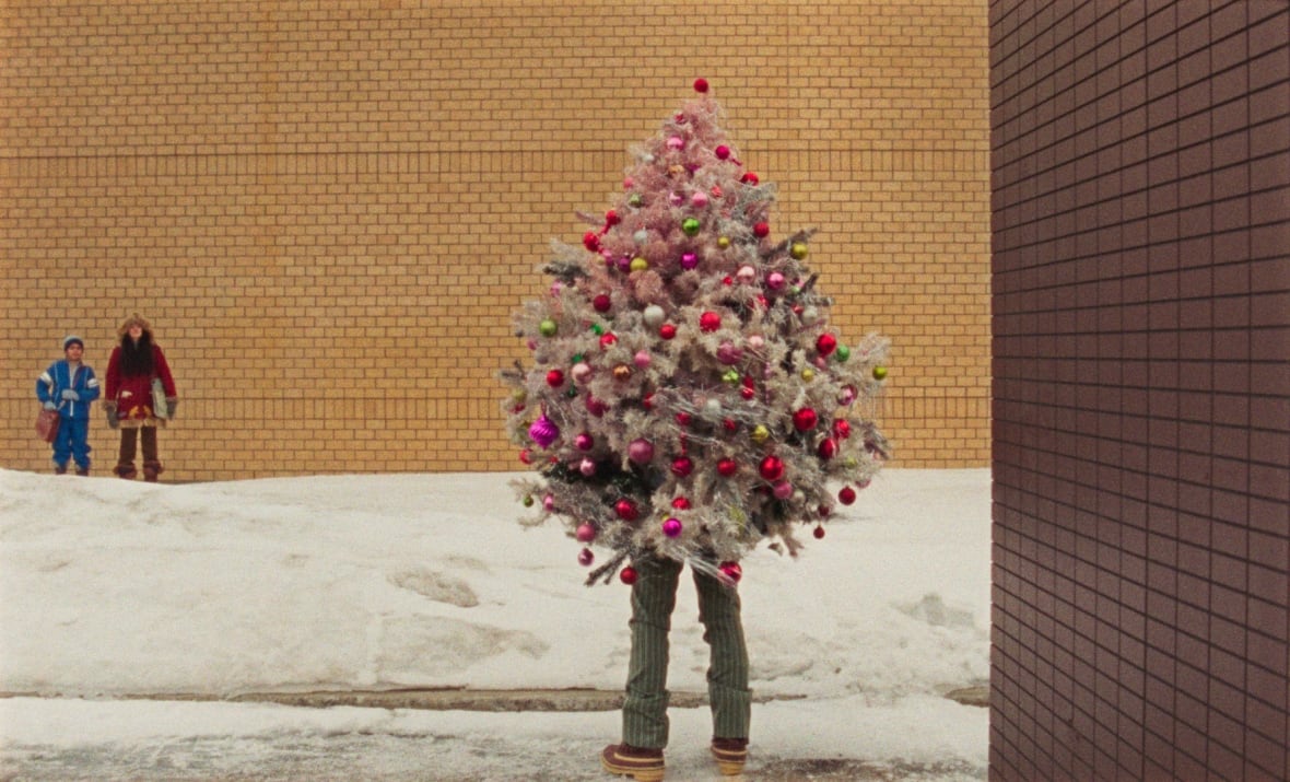 A still from a movie shows a person dressed up as a brightly coloured Christmas tree.