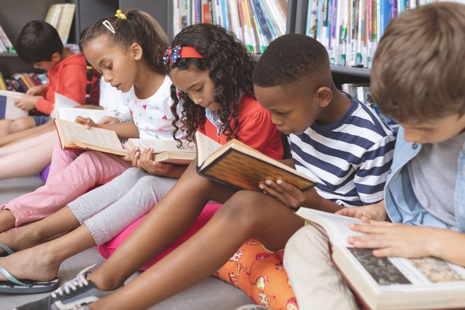 Children sitting on the floor in a library, reading books.