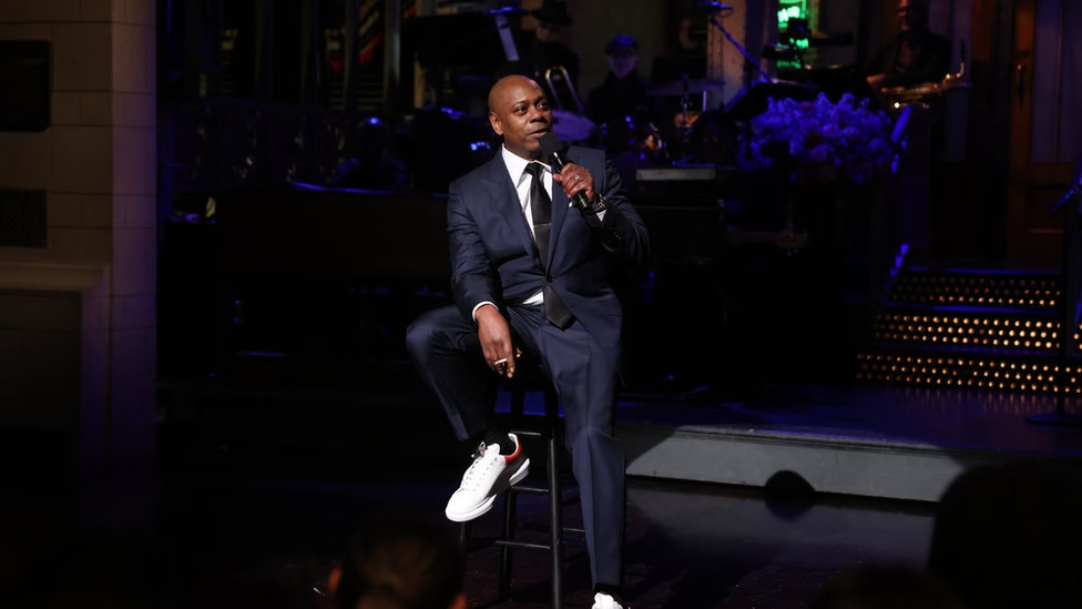 Dave Chappelle sits on a stool to deliver his SNL monologue