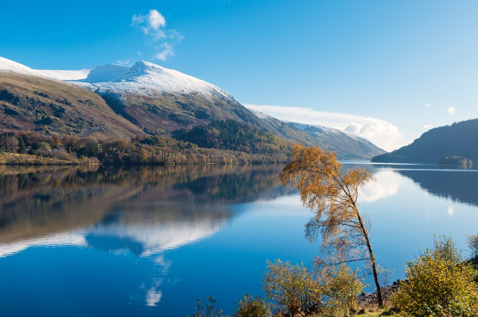 Snow-capped Helvellyn mountain reflected in a calm lake.