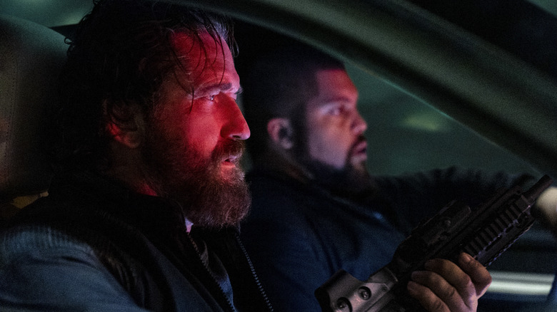 Big Nick and Donnie sit in the front seat of a car, their faces bathed in red light, in Den of Thieves 2: Pantera