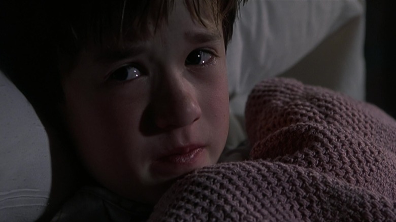 Haley Joel Osment as Cole Sear, clutching a blanket in bed with tears in his eyes in The Sixth Sense