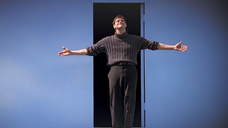 Jim Carrey as Truman Burbank, standing arms stretched in front of the exit door in The Truman Show