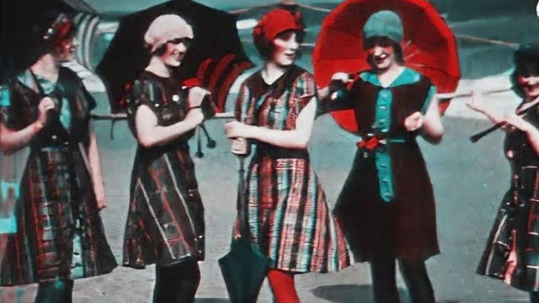 A group of five women from the 1900s wearing dresses, smiling, and carrying umbrellas from A Visit to the Seaside