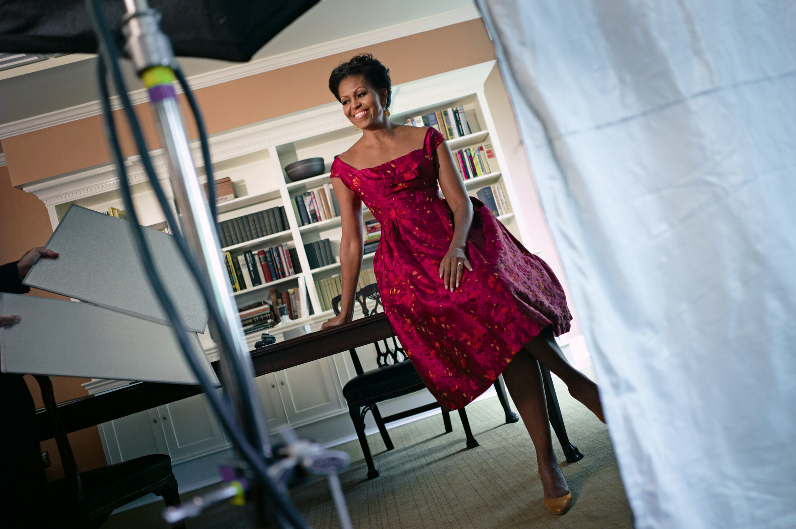 Michelle Obama in a red dress smiling behind photo equipment.