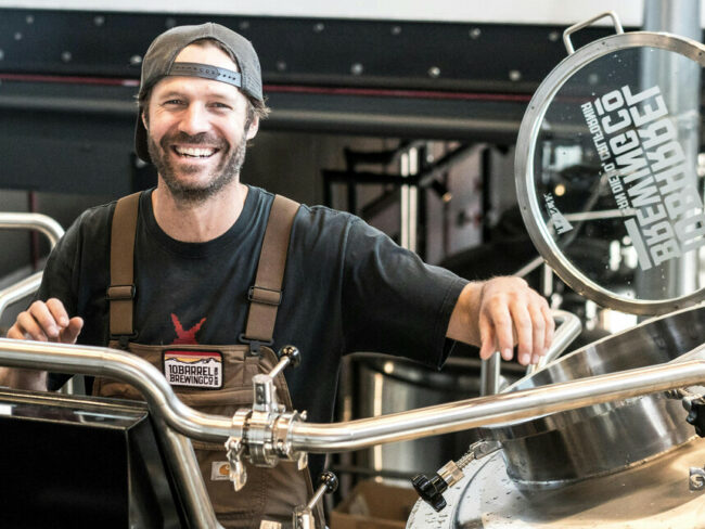 A-smiling-man-standing-near-metal-brewing-tanks-embodying-the-passion-behind-craft-beer.jpg