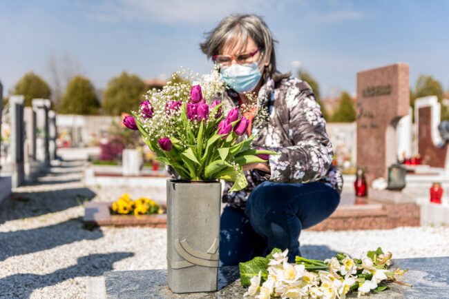 OlderLadyVisitingGraveWithSurgicalMask.jpg