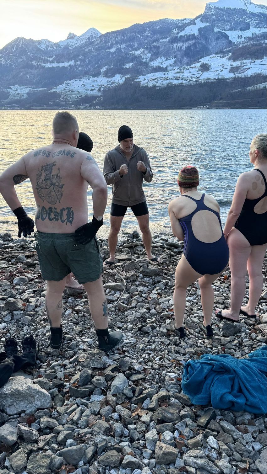Image of François Haman speaking with people in swimsuits in front of a lake with snowy mountains in the background. Image of François Haman speaking with people in swimsuits in front of a lake with snowy mountains in the background.