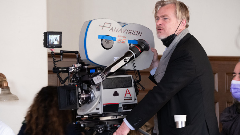 Director Christopher Nolan standing behind a camera in a behind-the-scenes still from the set of Oppenheimer