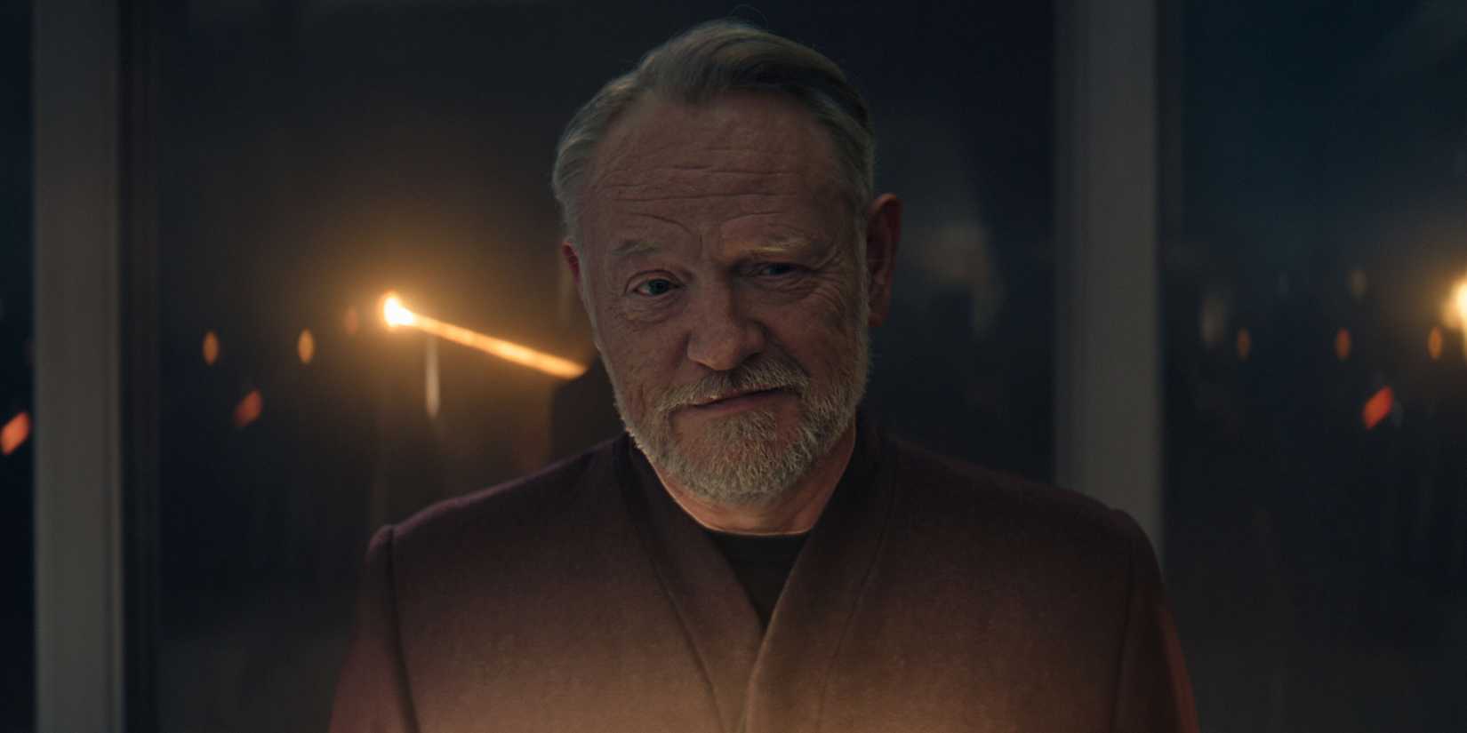 Jared Harris as Hari Seldon smirking and standing in front of a gladd window, away from it, in Foundation