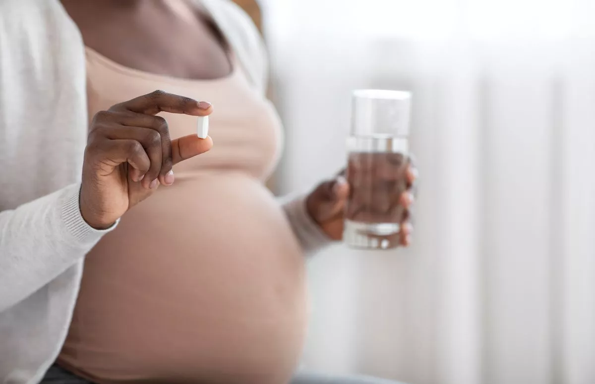 Supplements During Pregnancy. Unrecognizable Black Expectant Lady Holding Pill In Hand And Glass Of Water, Taking Maternity Vitamins For Health, Cropped Image With Selective Focus, Closeup