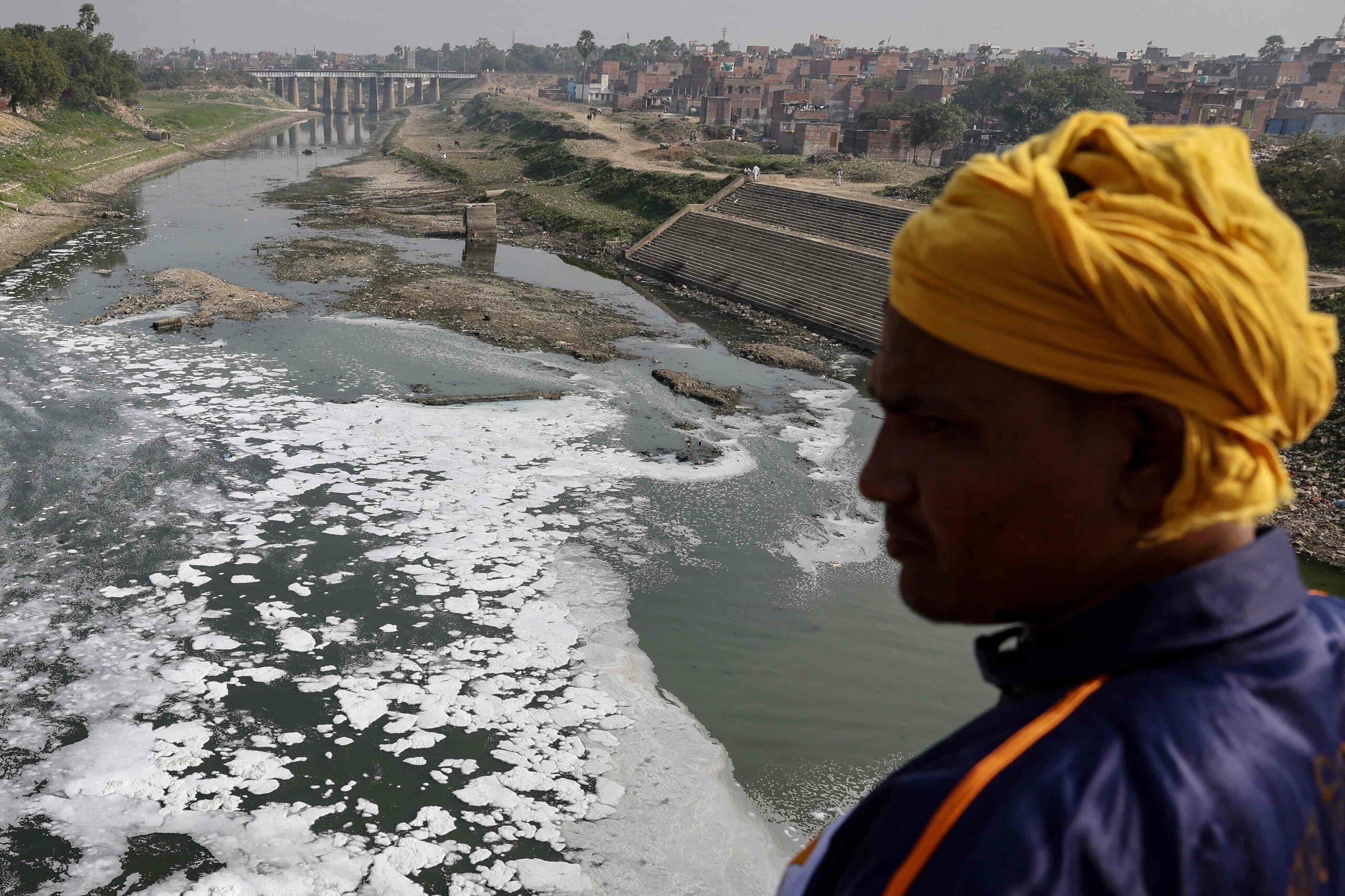 A man stands near the polluted Varuna River laden with toxic foam in Varanasi in December 2025. Credit: AFP.