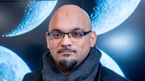 University of Leeds/Mark Bickerdike A headshot of Imad Ahmed. He is bald with a black and grey moustache and goatee beard. He is wearing glasses and a grey scarf.