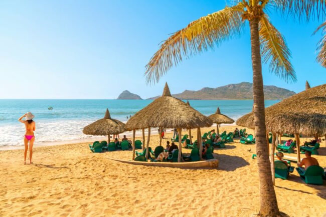 Tourists-enjoy-a-private-resort-club-with-straw-hut-cabanas-along-the-sandy-Playa-Gaviotas-beach-in-the-Golden-Zone-of-Mazatlan-Mexico-along-the-Sinaloa-Riviera.jpg