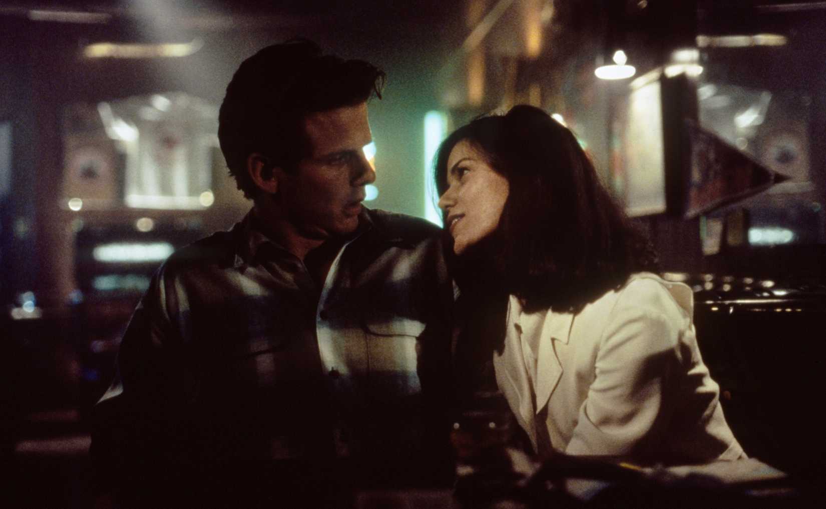 Peter Berg looks startled as Linda Fiorentino, smiling, sticks her hand down his pants in a booth in a bar in The Last Seduction