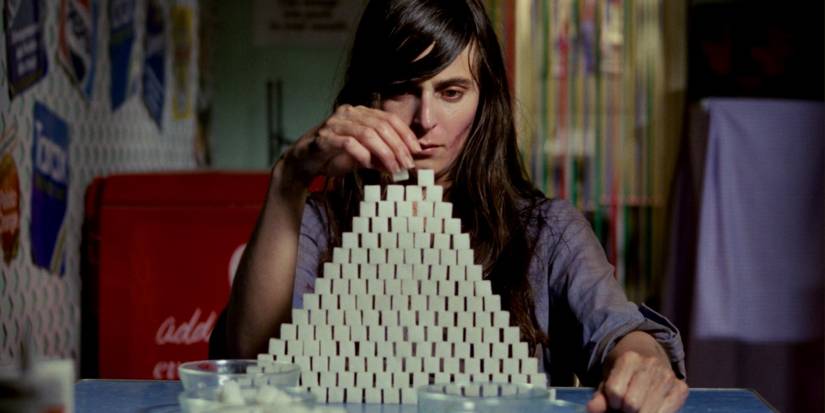 A woman building a pyramid of sugar cubes in Next of Kin
