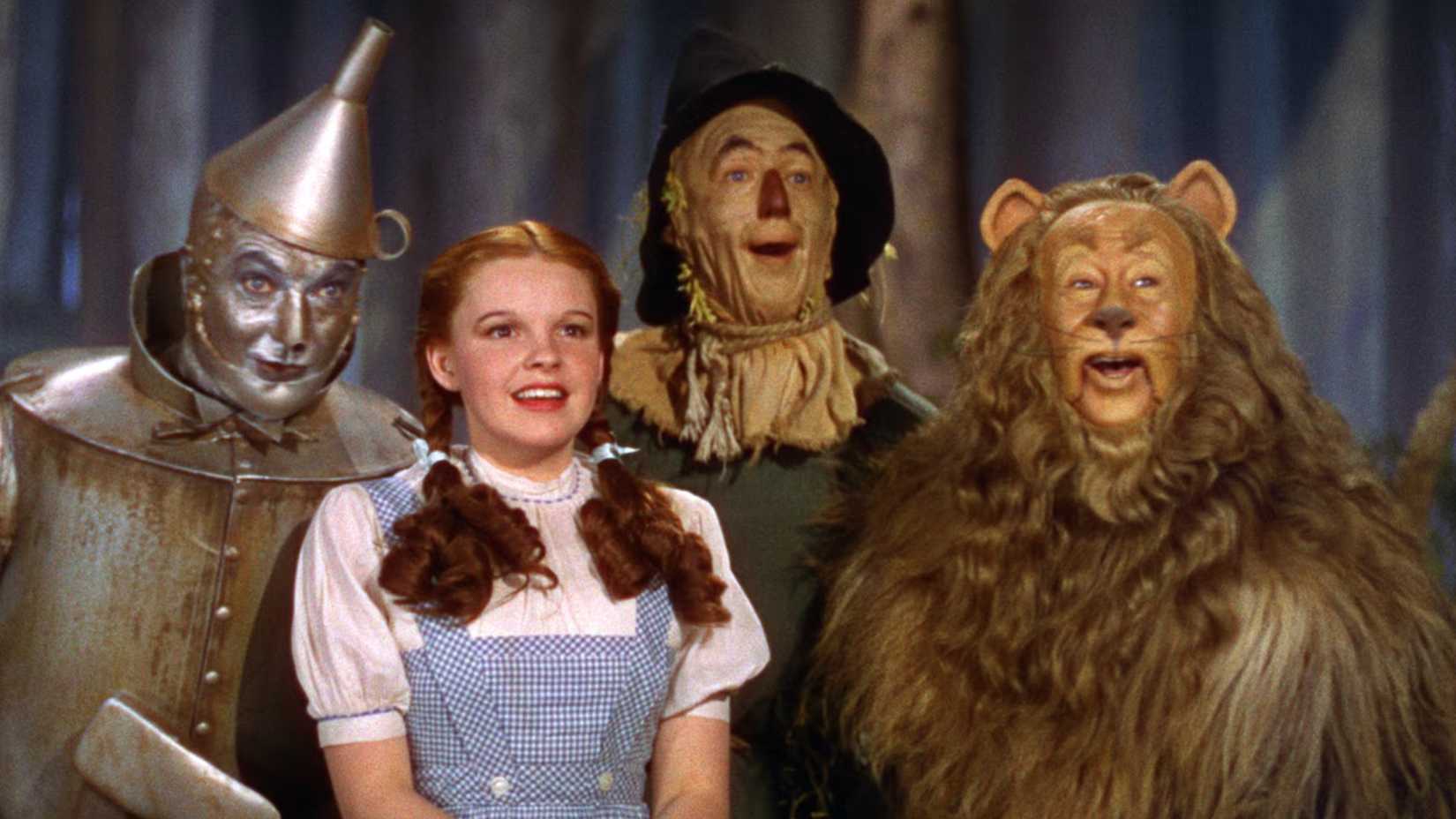 Dorothy, the Tin Man, Scarecrow, and the Cowardly Lion all smile in The Wizard of Oz