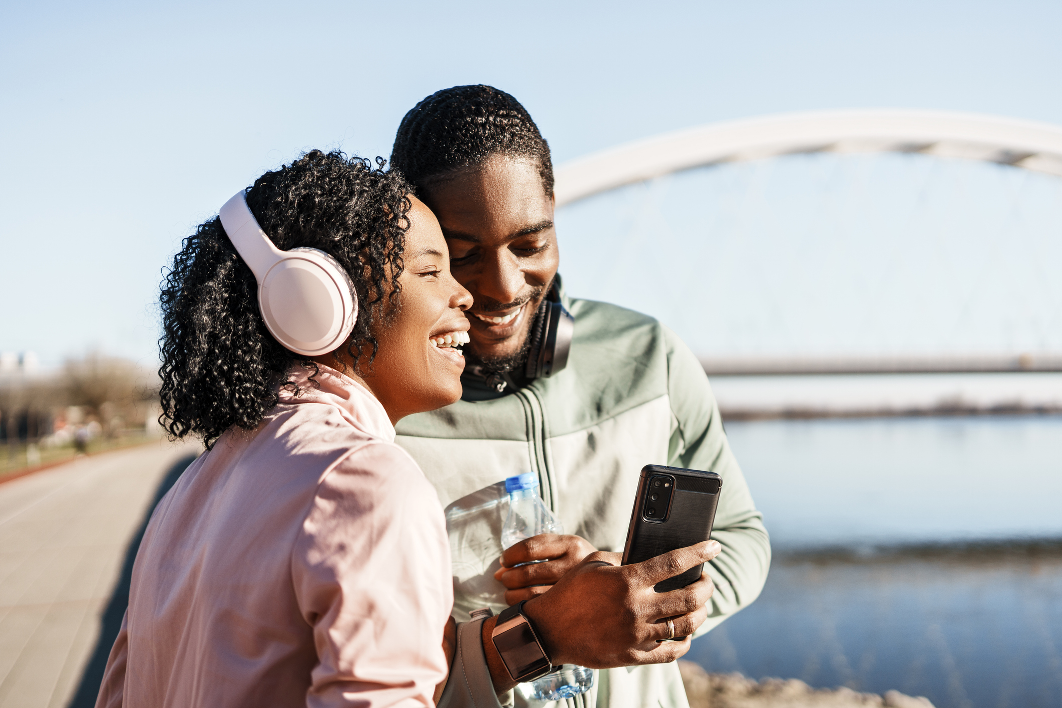 Woman and man with headphones, both smiling, near body of water