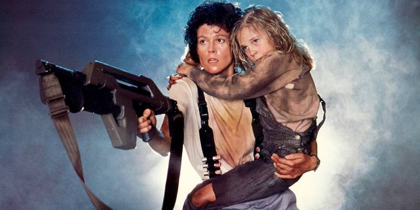 Ellen Ripley (Sigourney Weaver) points a gun while holding Newt (Carrie Henn) in Aliens.