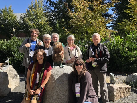 A group of people pose around a small bronze beaver sculpture.