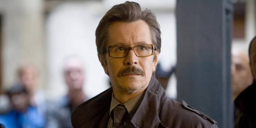 James Gordon stands in a suit and coat, looking up through his glasses with dread in 'The Dark Knight' (2008).