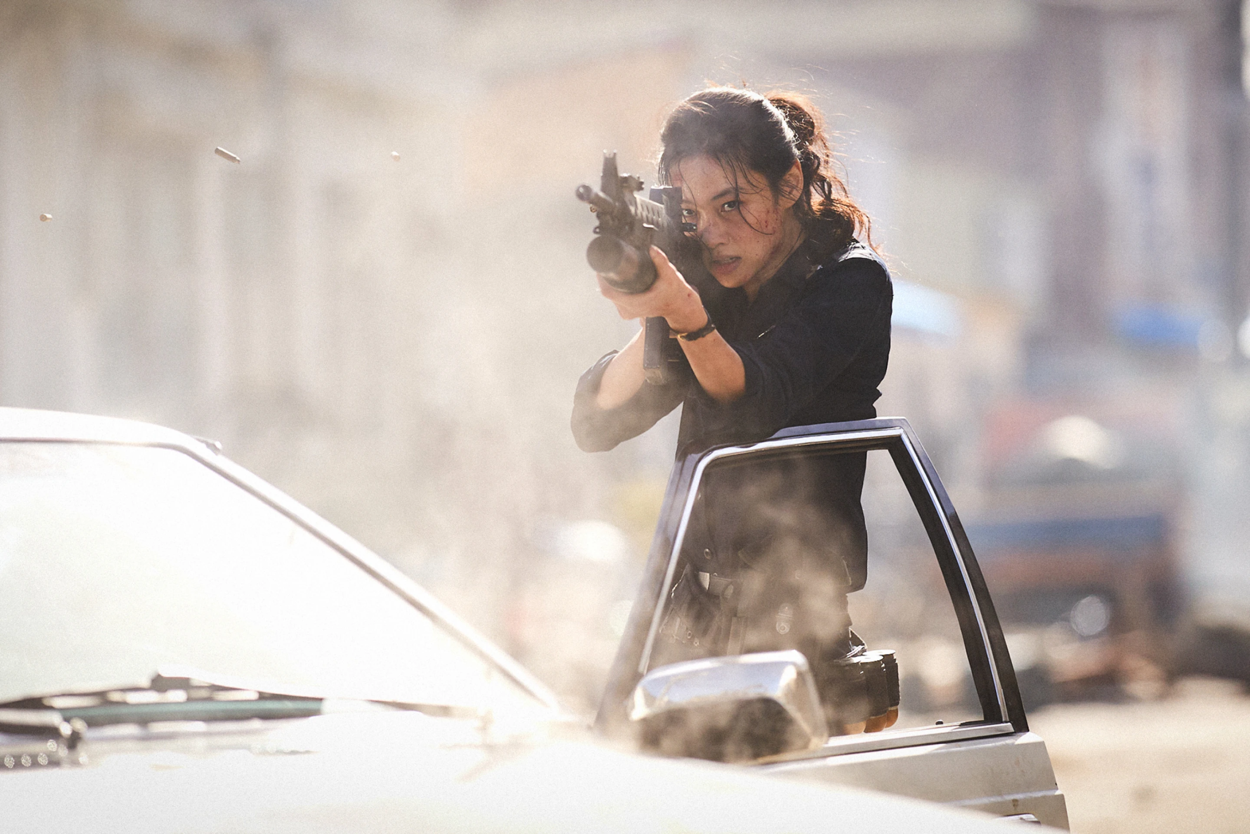 a woman standing behind a car door with a weapon aimed at the camera