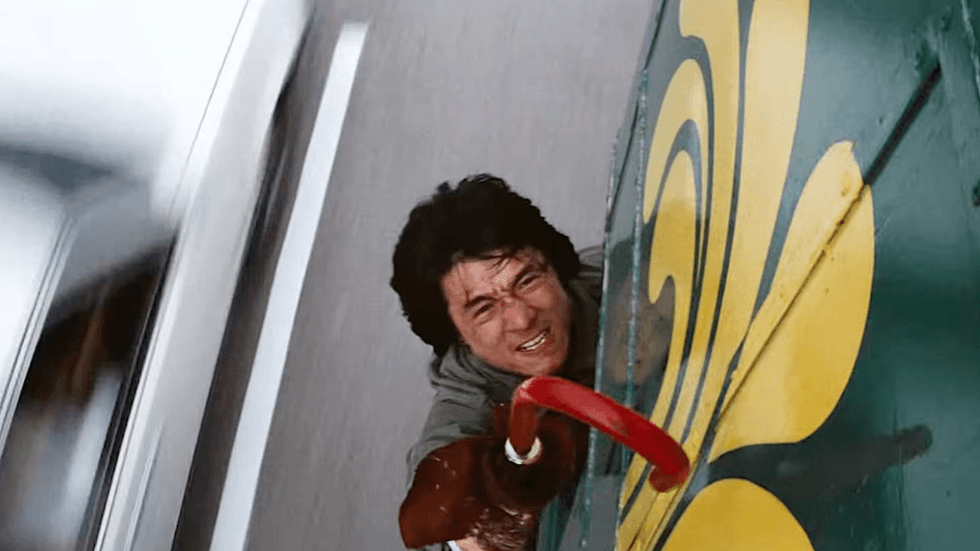 Jackie Chan performing a dangerous stunt hanging from the side of a bus in the 1985 action film Police Story